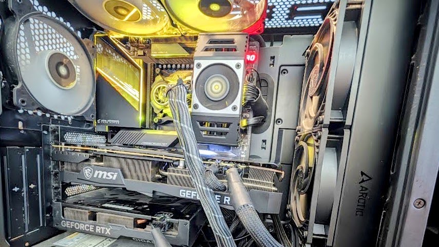 The inside of an open desktop computer case with an MSI GeForce RTX 3090 installed above a Gigabyte GeForce RTX 4060 Ti, a yellow-lit motherboard, and Arctic case fans.